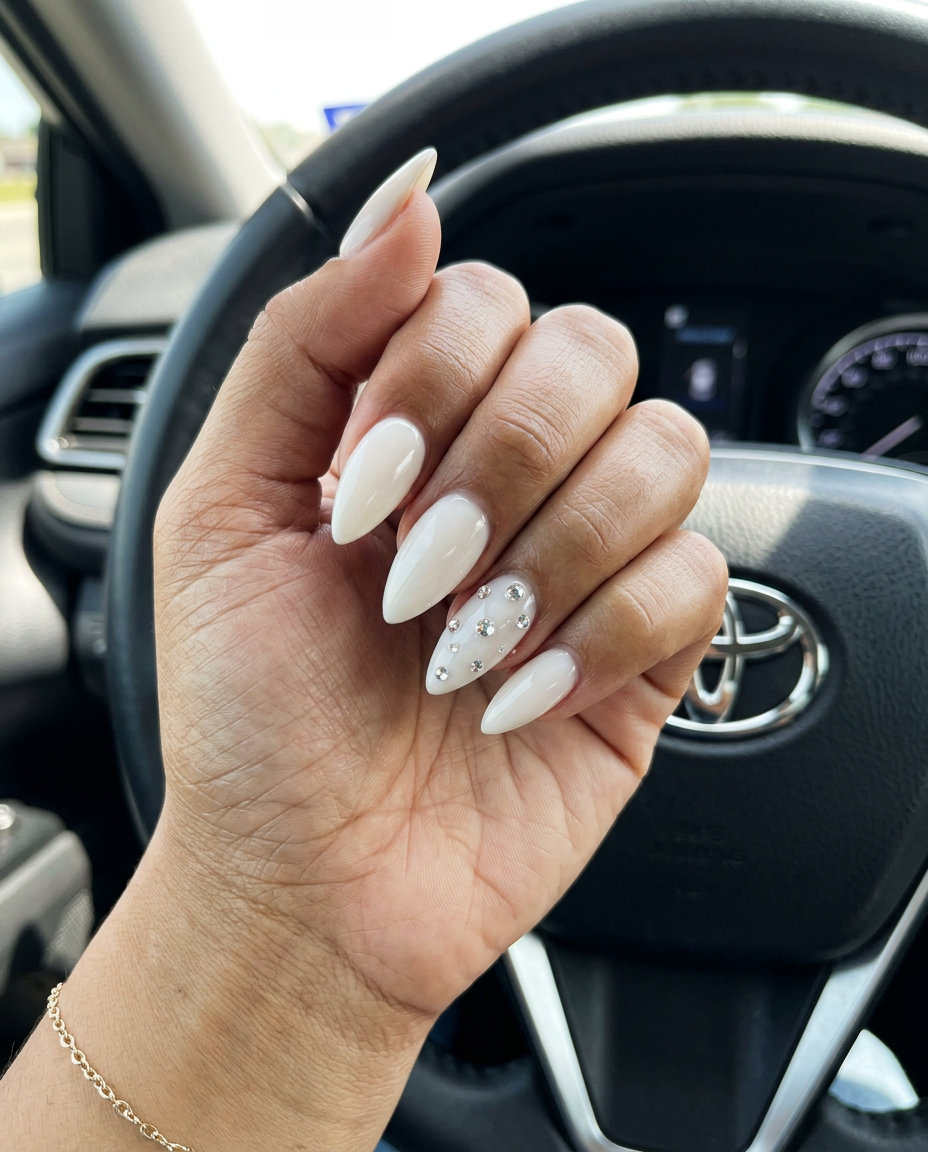 Milky white stiletto nails adorned with clear crystal rhinestones for a glamorous look. Stiletto summer nails 2026.